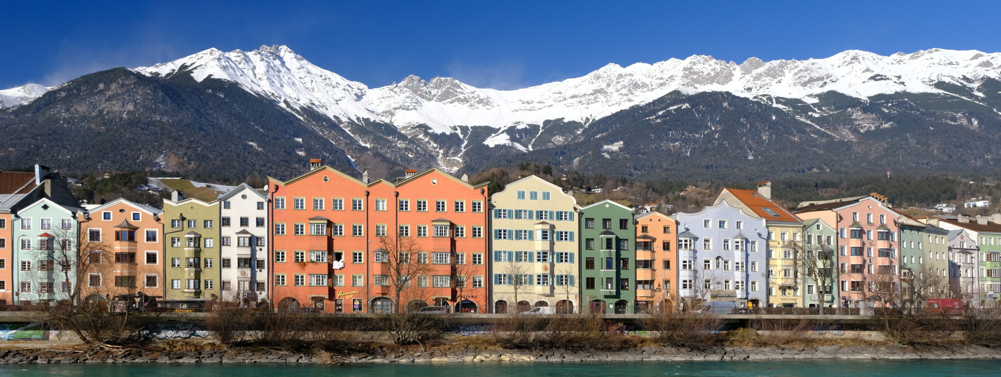 landscape format; row of coloured houses along the river; in the background snow capped mountains, blue sky