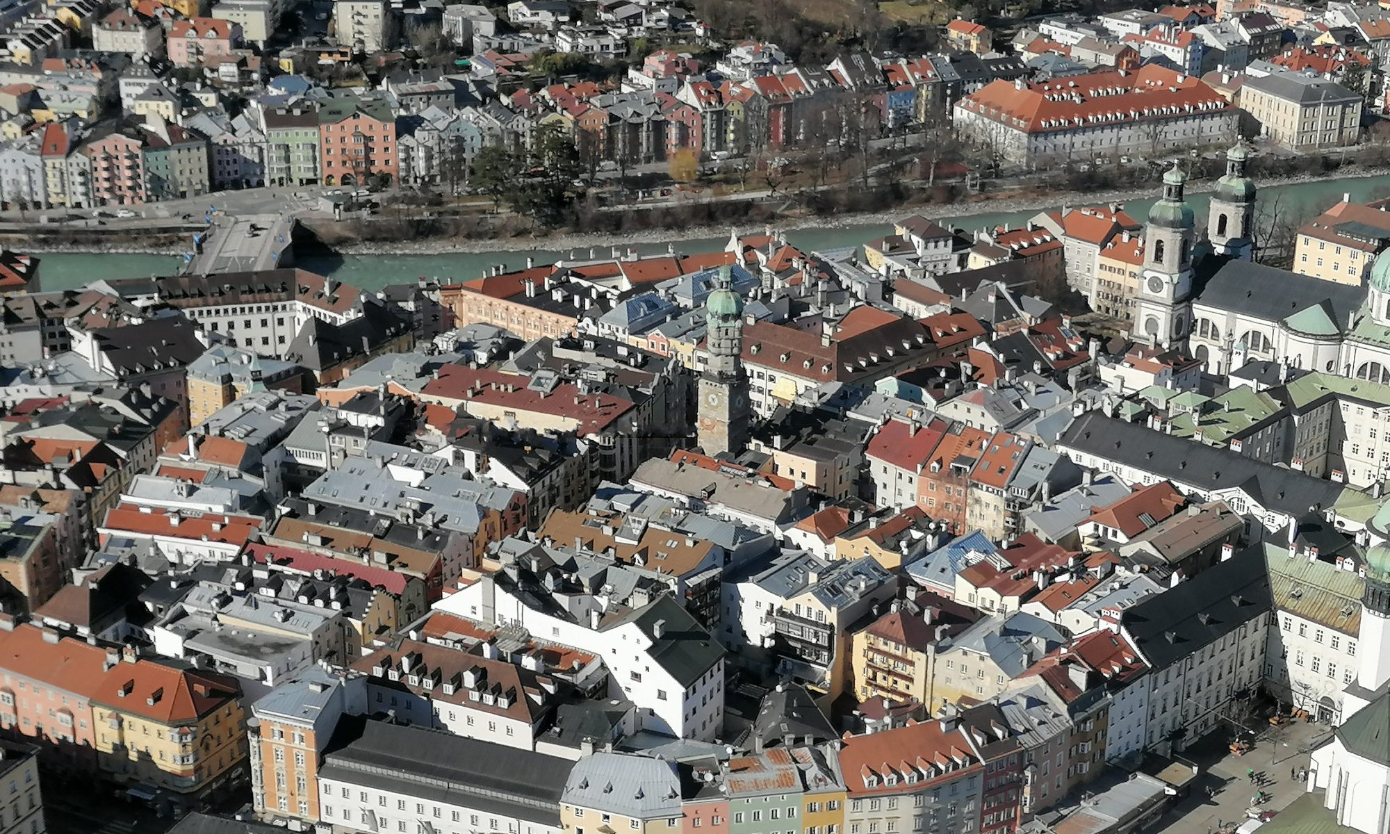 Landscape format; aerial view of the old town of Innsbruck, sunny day, lots of houses from above; in the upper third there is the river Inn, behind it the famous panorama of Mariahilf with the row of coloured houses.