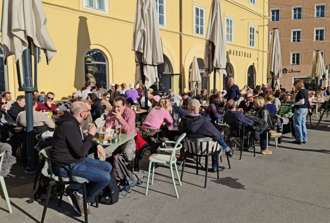 Landscape format; sunny day, open air cafe with many tables and many people