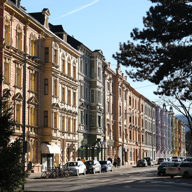 Quadrdatisches Format; Häuserzeile mit Fassaden in Pastellfarben, volle Bildhöhe im Vordergrund auf der linken Seite, perspektivisch kleiner werdend nach rechts.