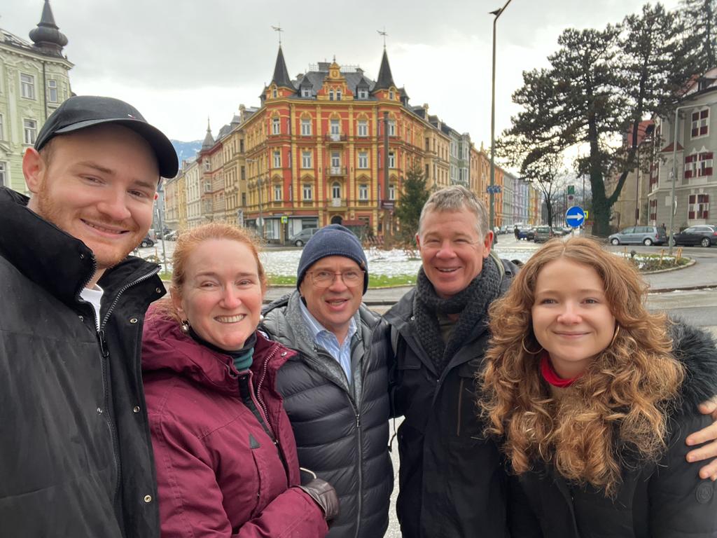Landscape format, selfie, 3 men and 2 women; parents and greeter in their 50ies, 60ies, children mid-20ies. Winter; big house with red and yellow facade in the background, grey sky.