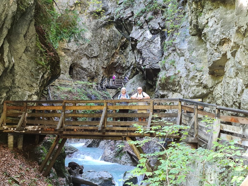 landscape format; rocky gorge, wooden bridge over the stream, man and woman standing on the bridge, looking towards the camera