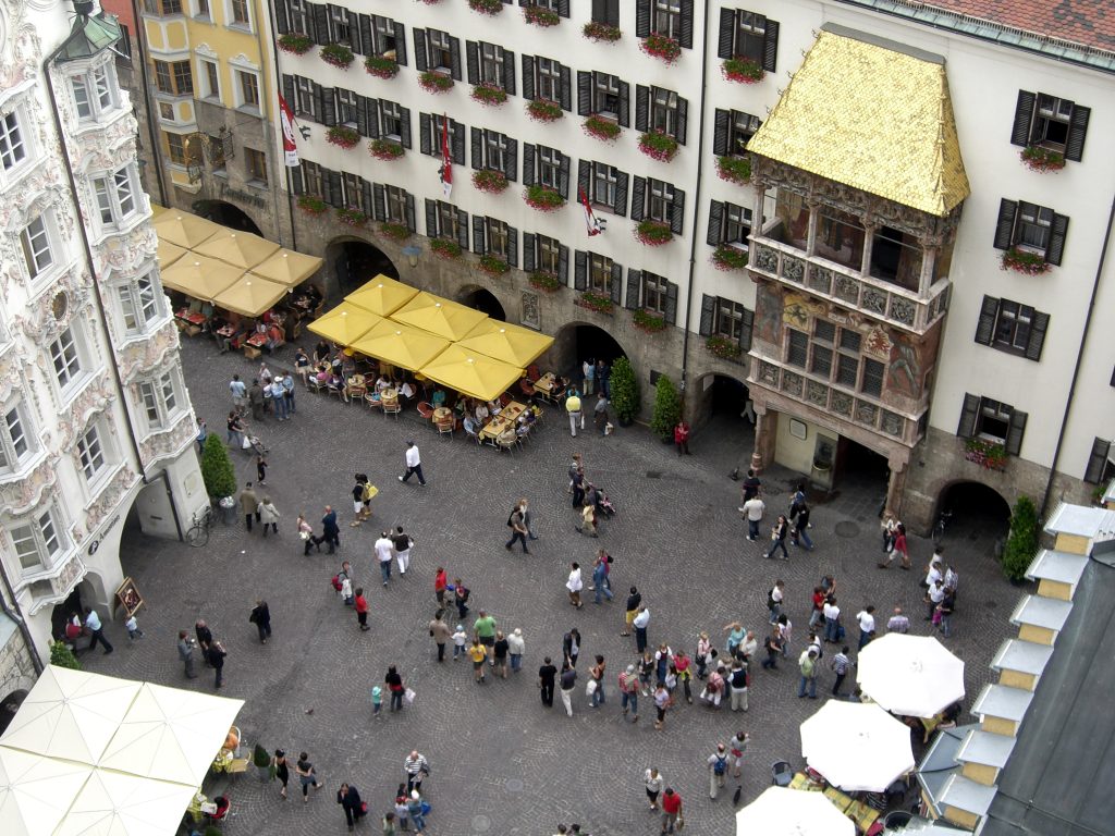 Landscape format; view from above (taken from the city tower); square with many people; outdoor cafes with sunshades; white building with portico and golden roof