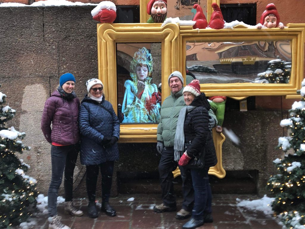 Querformat; 4 Personen in winterlicher Kleidung stehen im Freien vor zwei goldenen Rahmen mit Spiegeln