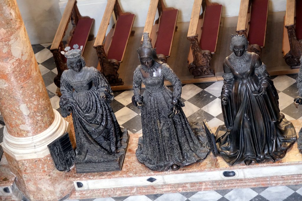 landscape format; view from the top; 3 female bronze statues (all turned black), fancy clothes