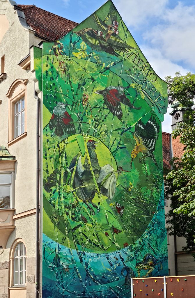 portrait format; big house wall, no windows; completely covered with a painting mostly in green; birds, insects and plants