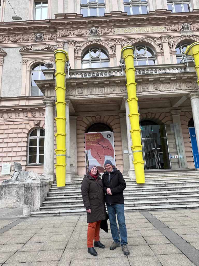 portrait format; a woman and a man standing in front of a building (museum)