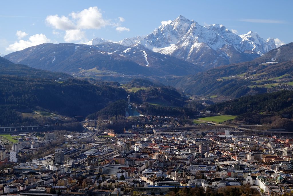 landscape format: city with lots of houses, aerial view; from the vertical center to the top there's first the green hills (lots of trees), then a big snow covered mountain