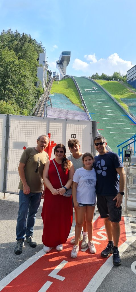 Portrait format; a group of 5; man in brown T-shirt, woman in red dress, sunglasses, male and female children, man in blue T-shirt and shorts, sunglasses