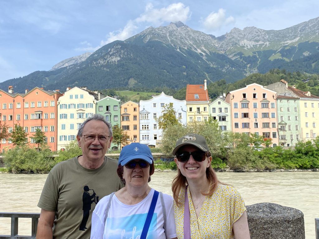 landscape format; 3 people in front of the row of colourful houses, the river inbetween, mountains in the background